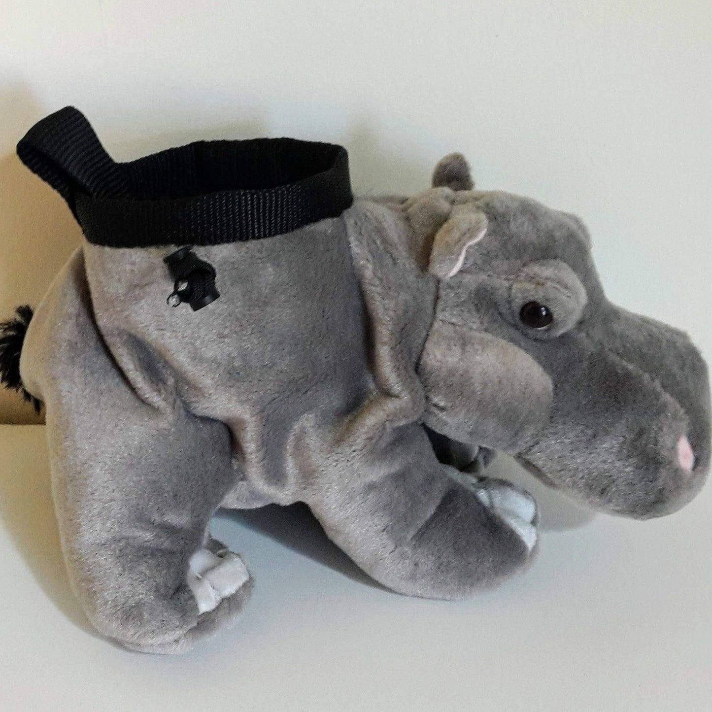 A plush hippopotamus chalk bag in grey fabric, designed to look like a soft toy, with a black webbing rim and drawstring closure, positioned on a light surface against a white background.