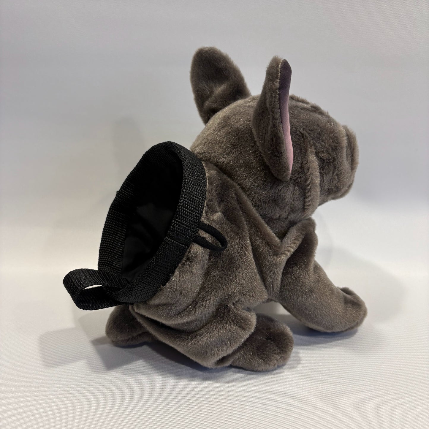 Grey boxer dog plush rock climbing chalk bag, pictured slightly from the rear, showing the chalk bag section with a polypropylene rim, on a white background